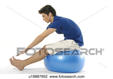 Stock Image - Side profile of a young man sitting on a fitness ball and exercising. Fotosearch
