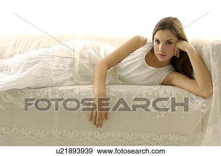 Stock Photo - Portrait of a young woman lying on a couch with her head in her hand. Fotosearch