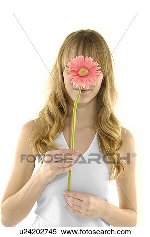 Stock Photography - Close-up of a young woman holding a flower in front of her face. Fotosearch