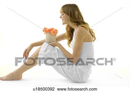 Stock Image - Side profile of a young woman holding a flower pot. Fotosearch