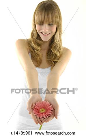 Stock Image - Young woman holding a flower and smiling. Fotosearch