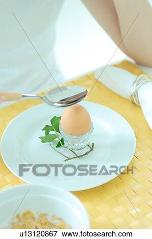 Stock Photo - Unrecognizable woman tapping boiled egg with spoon. Fotosearch