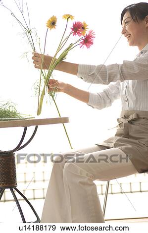 Stock Photo - A young woman arranging flower, side view. Fotosearch