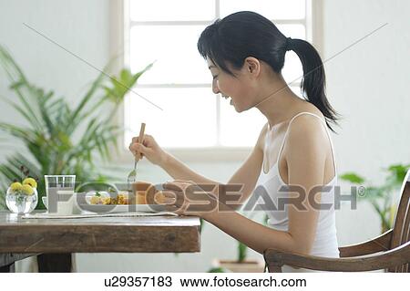 Stock Image - A young woman eating breakfast. Fotosearch