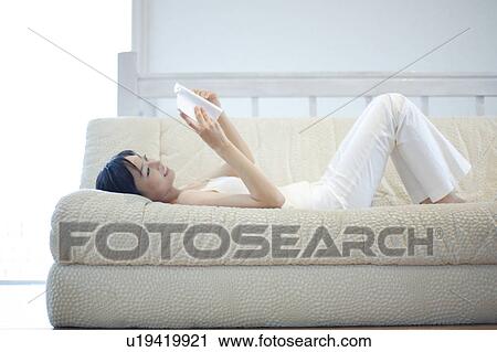A young woman reading a book lying in sofa View Large Photo Image Stock Image - A young woman reading a book lying in sofa. Fotosearch