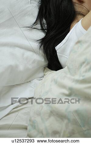 Stock Image - A young woman sleeping in bed, rear view. Fotosearch