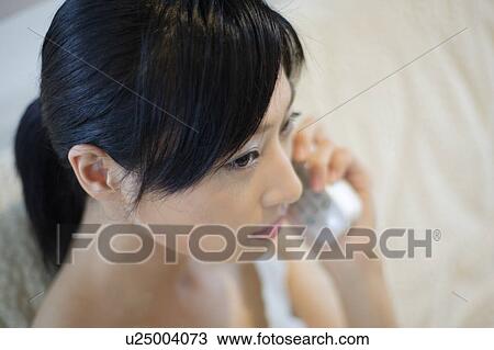 Stock Image - A young woman talking over phone, close-up. Fotosearch