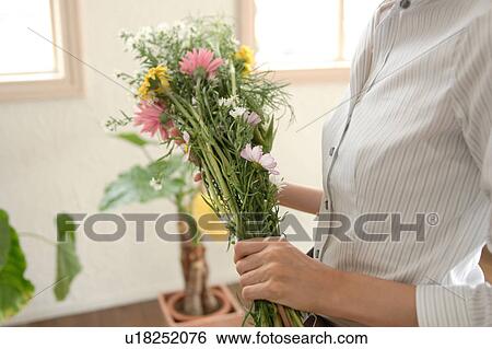 Stock Photograph - Midsection of a young woman holding flower. Fotosearch