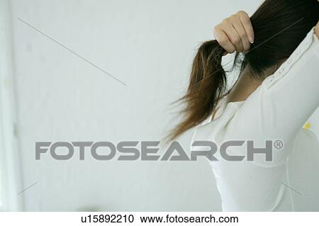 Stock Image - A young woman holding hair, side view. Fotosearch
