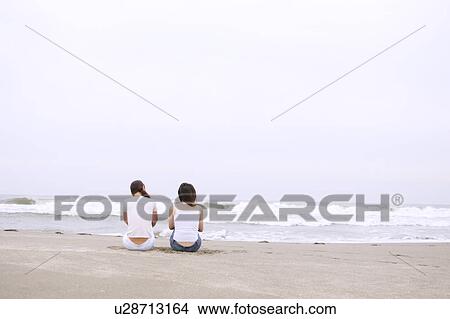 Two young women sitting at beach View Large Photo Image Picture - Two young women sitting at beach. Fotosearch