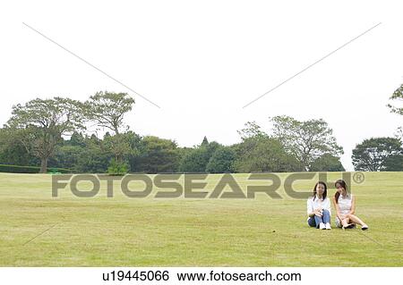 Two young women sitting in park View Large Photo Image Stock Photograph - Two young women sitting in park. Fotosearch