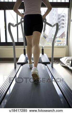 Stock Photography - Rear view of young woman walking on treadmill in gym. Fotosearch