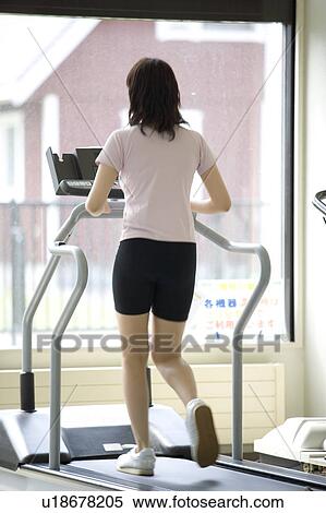 Stock Photography - Rear view of young woman walking on treadmill in gym. Fotosearch