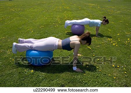 Two young women doing push-ups with their legs on fitness balls View Large Photo Image Stock Photo - Two young women doing push-ups with their legs on fitness balls. Fotosearch