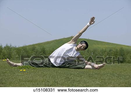 Stock Image - Young man doing the splits in field. Fotosearch