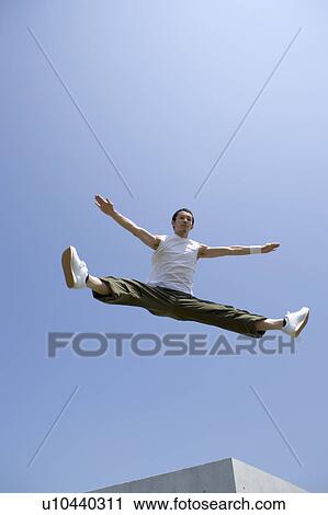 Stock Image - Young man jumping and doing splits in mid air. Fotosearch