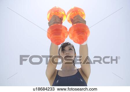 Stock Image - Young woman exercising with dumbbells. Fotosearch