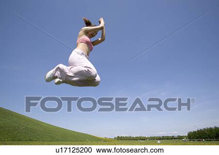 Stock Image - Young woman jumping in field. Fotosearch