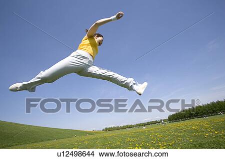 Picture - Young woman leaping in field. Fotosearch