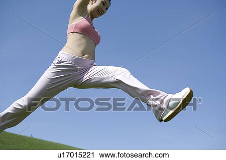 Stock Image - Young woman leaping in field. Fotosearch