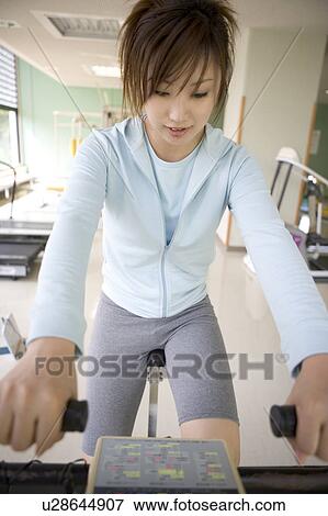 Stock Photo - Young woman riding exercise bike in gym. Fotosearch