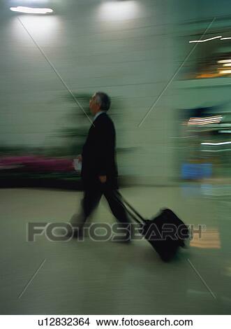 Businessman walking with luggage at airport, blurred motion View Large Photo Image Picture - Businessman walking with luggage at airport, blurred motion. Fotosearch