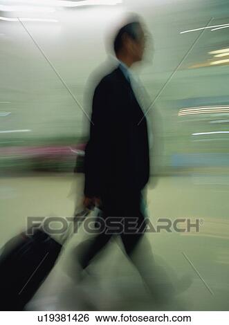 Stock Photograph - Businessman walking with luggage at airport, blurred motion. Fotosearch