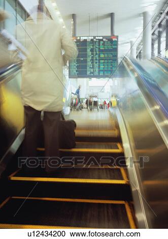 Stock Image - Man going up on escalator at airport, blurred motion. Fotosearch