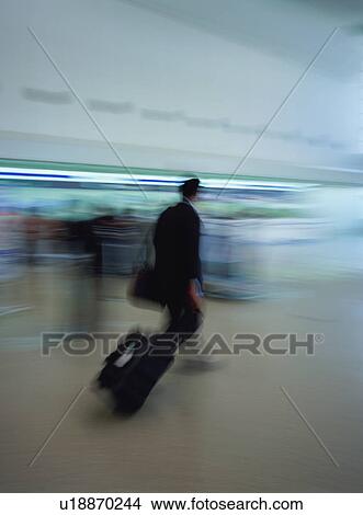 Picture - Man walking with luggage at airport, blurred motion. Fotosearch