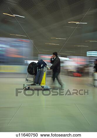 Stock Image - Man walking with luggage at airport, blurred motion. Fotosearch