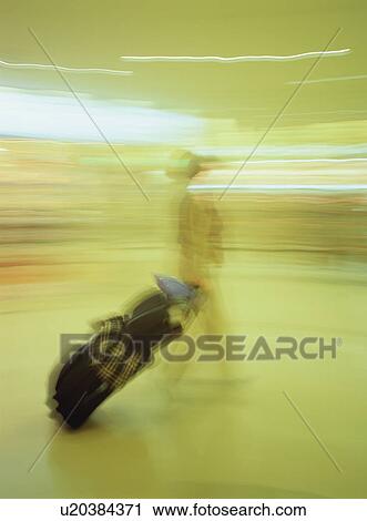 Stock Image - Traveler walking with luggage at airport, blurred motion. Fotosearch