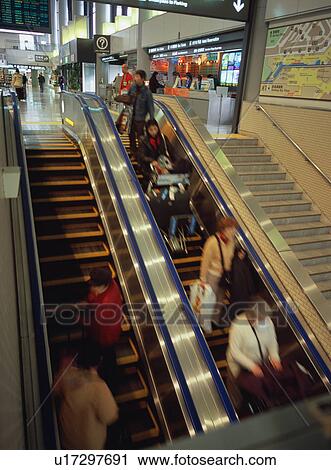Stock Image - Travelers on escalator at airport, blurred motion. Fotosearch