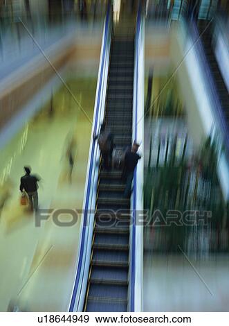 Stock Photo - Two travelers going up on escalator at airport, blurred motion. Fotosearch