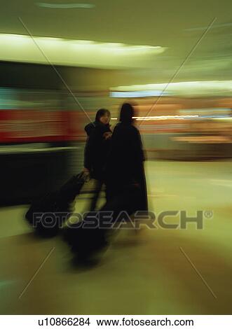 Two women walking with luggage at airport, blurred motion View Large Photo Image Picture - Two women walking with luggage at airport, blurred motion. Fotosearch