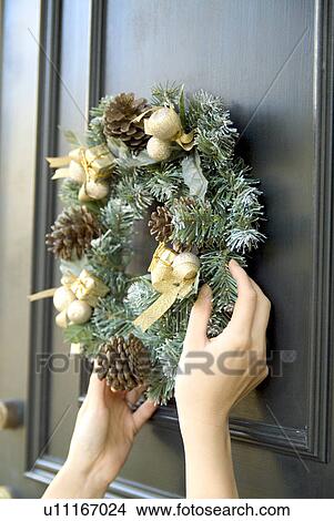 Picture - Person hanging Christmas wreath on door. Fotosearch