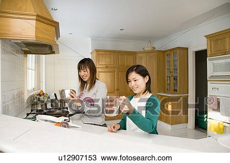 Stock Image - Two young women cooking in kitchen. Fotosearch