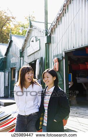 Stock Photo - Two young women standing in front of boathouse. Fotosearch