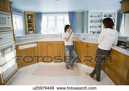 Two young women talking in kitchen View Large Photo Image Stock Photo - Two young women talking in kitchen. Fotosearch
