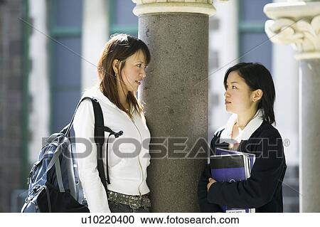 Two young women talking on campus View Large Photo Image Stock Image - Two young women talking on campus. Fotosearch