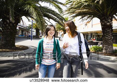 Two young women walking in a town View Large Photo Image Stock Photo - Two young women walking in a town. Fotosearch