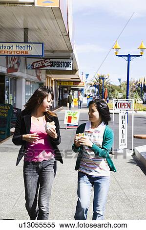 Stock Photography - Two young women walking with hamburgers in hands. Fotosearch