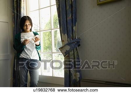 Stock Photo - Young woman reading a book by window. Fotosearch