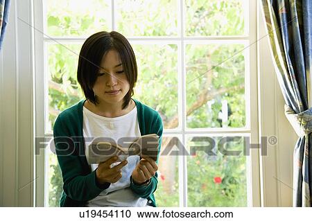 Young woman reading a book in front of window View Large Photo Image Stock Image - Young woman reading a book in front of window. Fotosearch