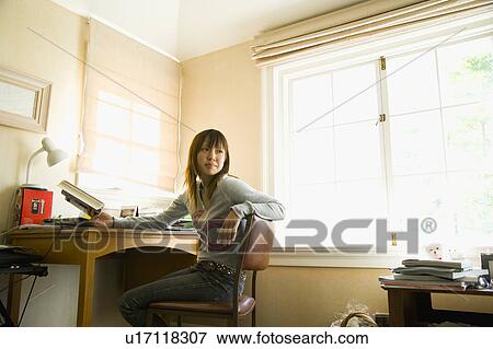 Young woman sitting at desk View Large Photo Image Stock Photo - Young woman sitting at desk. Fotosearch