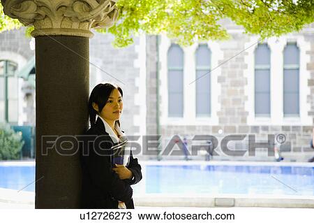 Stock Image - Young woman standing with textbook. Fotosearch