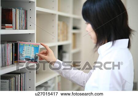 Stock Photo - A young woman selecting a CD from bookshelf. Fotosearch