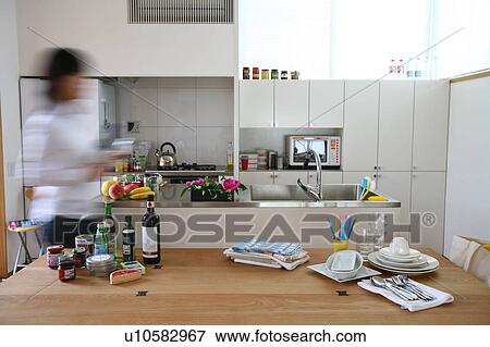 Stock Photo - A young woman walking in kitchen, blurred motion. Fotosearch