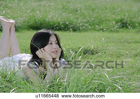 Stock Photo - A young woman lying on grass field. Fotosearch