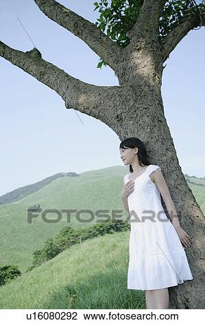 Stock Image - A young woman standing under tree. Fotosearch