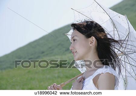Stock Image - A young woman standing with parasol. Fotosearch